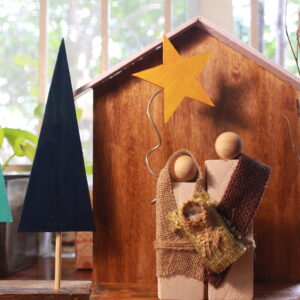 Handcrafted wooden Holy Family crib with Mary, Joseph, and Baby Jesus under a star, surrounded by minimalist wooden Christmas trees and warm fairy lights.