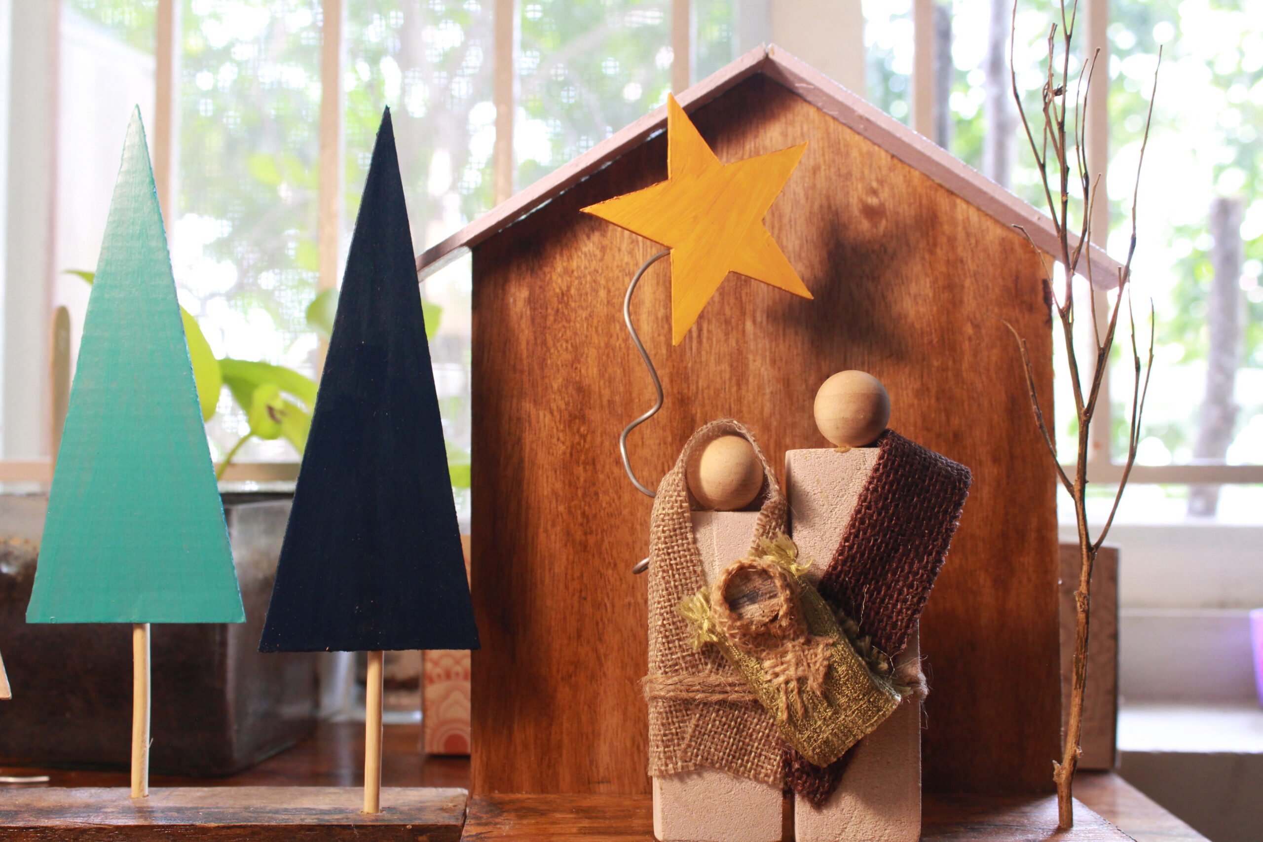Handcrafted wooden Holy Family crib with Mary, Joseph, and Baby Jesus under a star, surrounded by minimalist wooden Christmas trees and warm fairy lights.